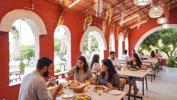 A restaurant with outdoor seating, red brick walls, and hanging lights. - Fabhotel Nakshtra Resort (Tasgaon)