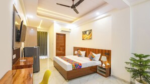 A hotel room with a bed, bedside table, lamp, TV, and a ceiling fan. - FabHotel 24x Living (Gurugram)