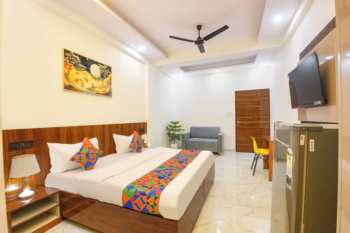A hotel room with a bed, a television, a desk, a chair, a plant, and a ceiling fan.
