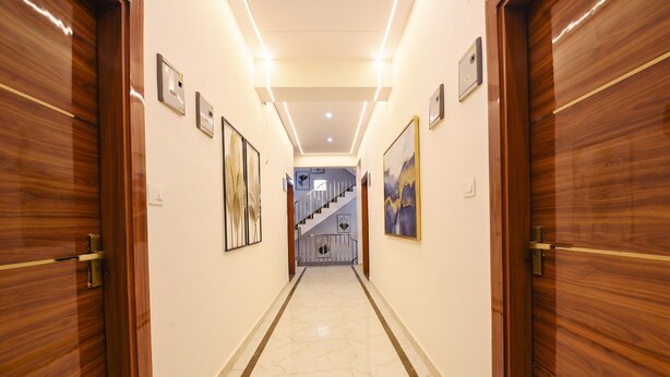 A hallway with wooden doors, framed artwork, and a marble floor leading to a staircase. - FabHotel 24x Living (Gurugram)
