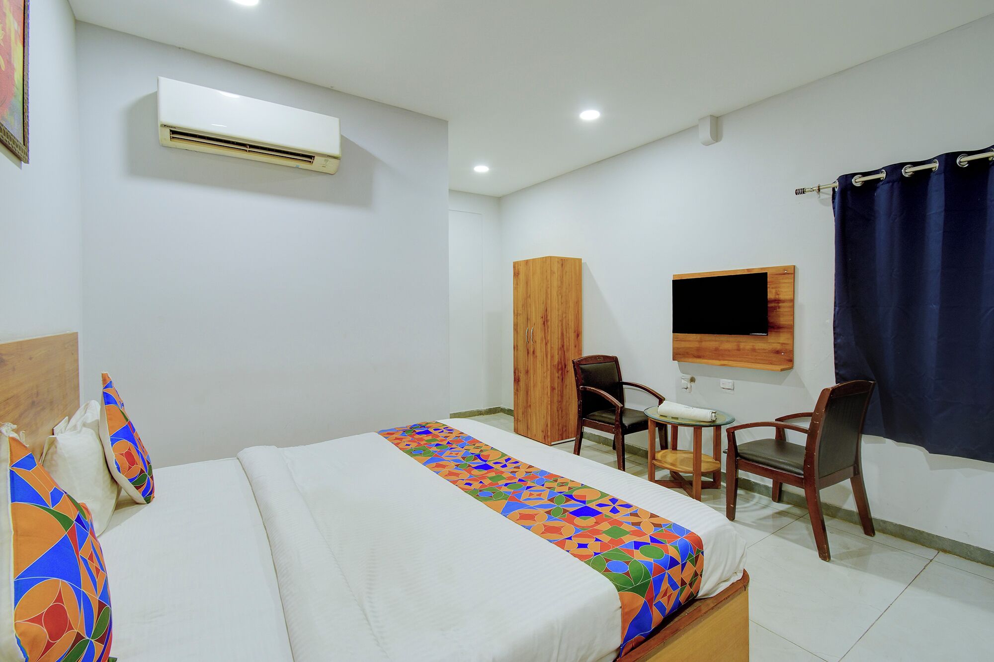 Habitación de hotel con cama, armario de madera, escritorio con silla, televisor montado en la pared y aire acondicionado.