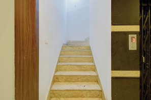 Una stretta scala con un telaio di legno a sinistra e un pannello di controllo dell'ascensore a parete a destra.