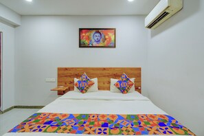 A bedroom with a wooden headboard, a bed with patterned pillows, a colorful bedspread, a wall-mounted air conditioner, and a framed artwork above the bed. - Fabhotel Vaishnavi Classic (Hyderabad)