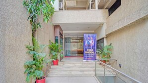 Entrada de hotel con barandilla de vidrio, plantas en macetas y un cartel publicitando un evento semanal.