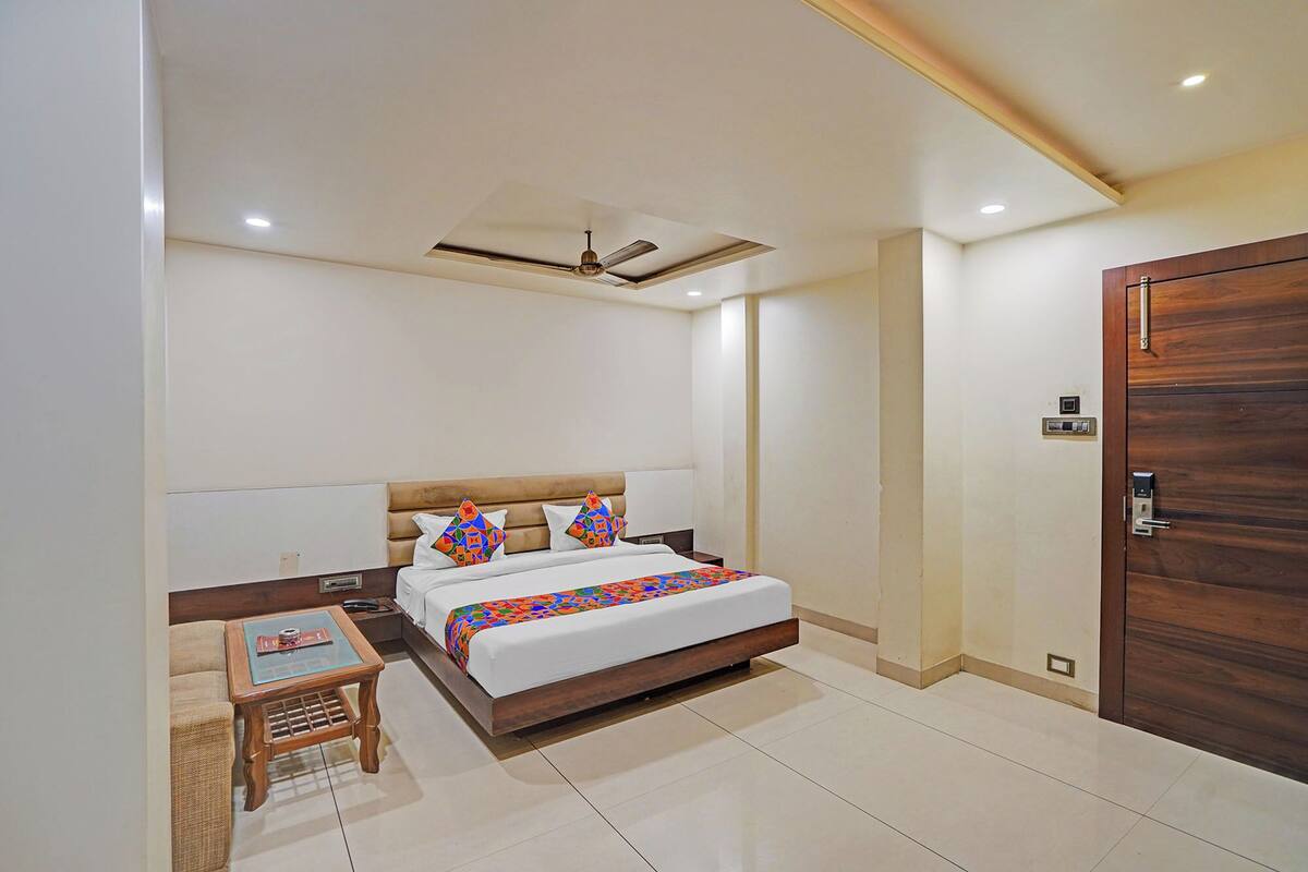 Une chambre d’hôtel avec un lit, une petite table, une chaise, une porte en bois et un ventilateur de plafond.