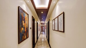 Un pasillo de hotel con obras enmarcadas en las paredes, suelo de mármol pulido e iluminación empotrada.