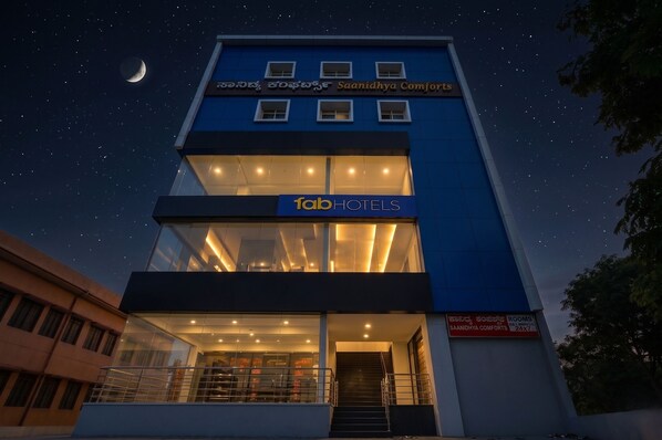 A modern building with a sign for 'fabHOTELS' and 'SAANIDHYA COMFORTS' indicating a hotel. - FabHotel Saanidhya Comforts - Tumkur Road (Kunigal)