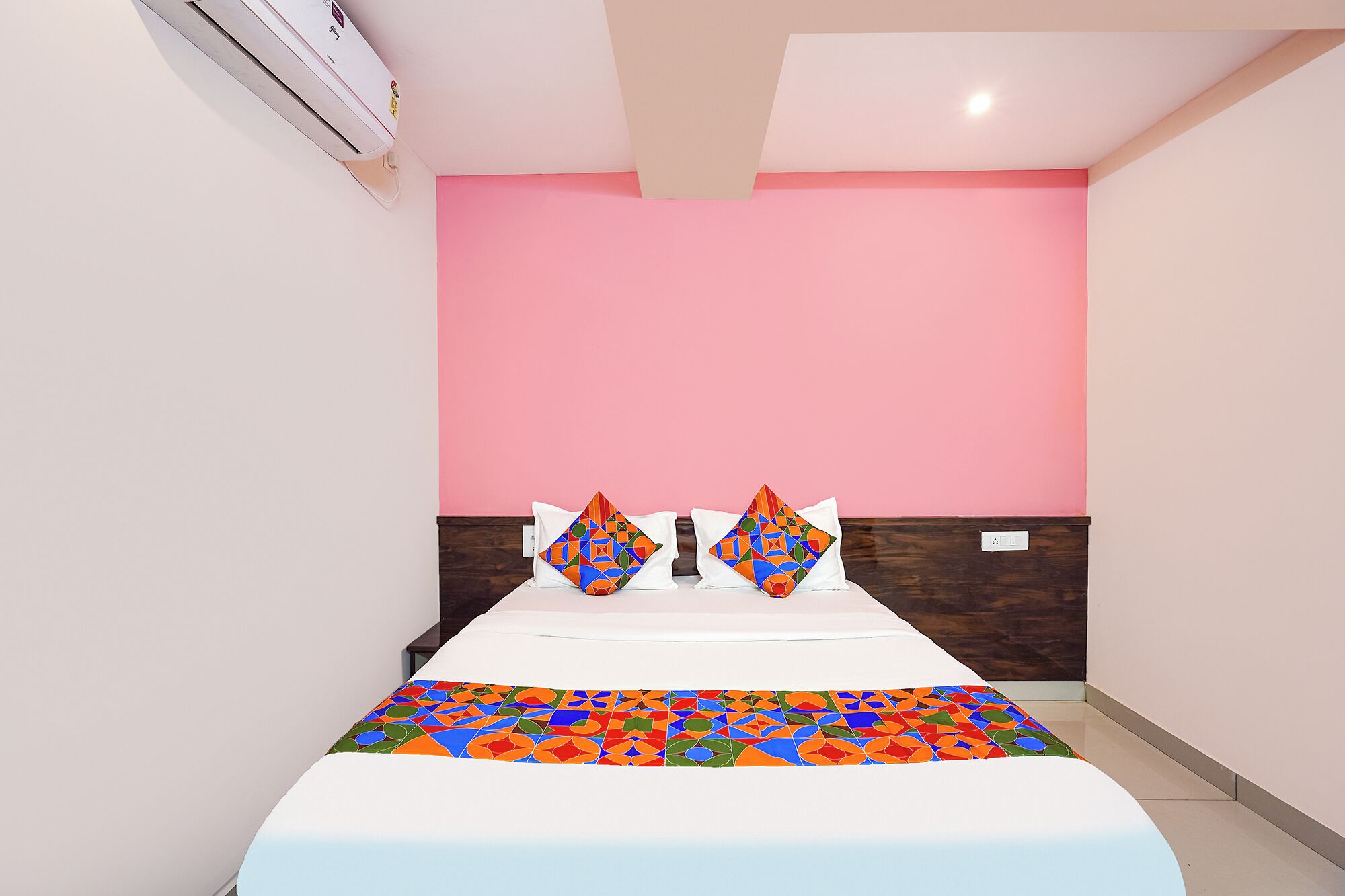 A hotel room with a bed, a pink wall, and a wooden headboard.