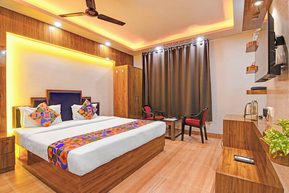 A hotel room with a bed, bedside tables, a desk with chairs, a TV, and a ceiling fan.