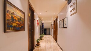 Um corredor de hotel com obras de arte emolduradas, plantas em vasos e piso de mármore.