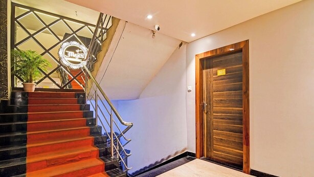 Uma escada com corrimão de metal, uma porta de madeira com placa de número e um vaso de planta.