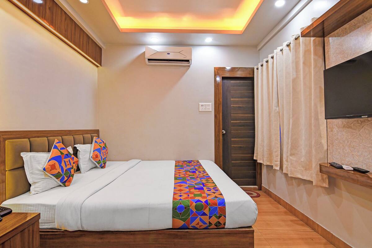 A hotel room with a bed, a TV, an air conditioning unit, and a door.