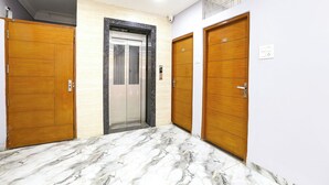 A hallway with marble flooring, wooden doors, and a central elevator. - FabHotel Suraj Palace (Indore)
