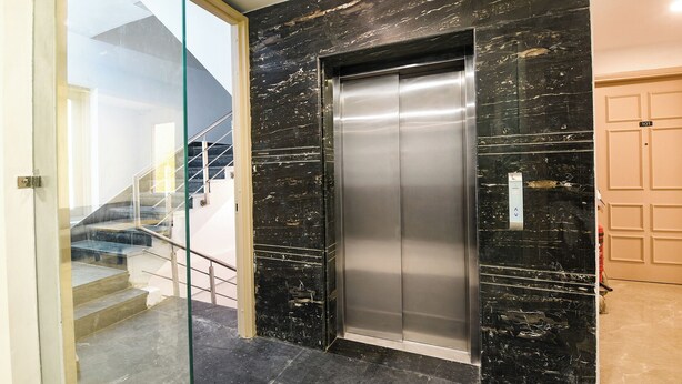 A modern elevator with a metallic finish, a glass door, and a marble wall. - Fabhotel Moro Gujranwala Town (New Delhi)