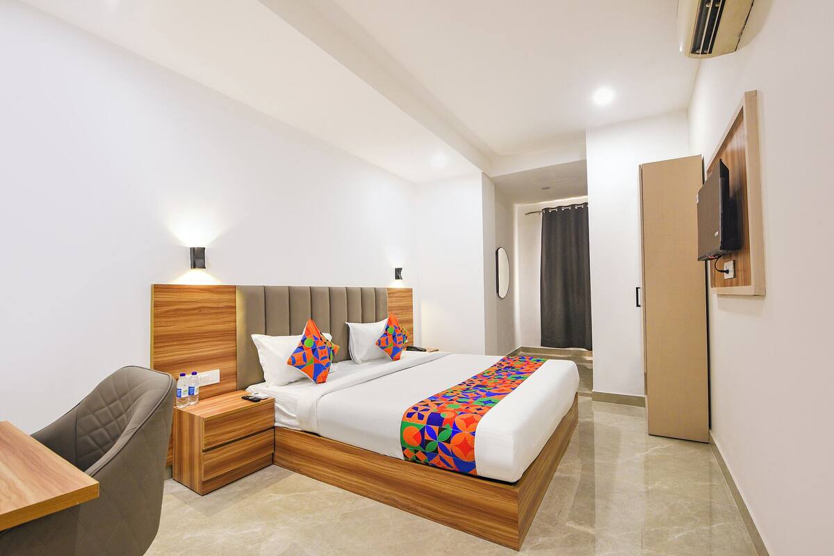 A hotel room with a bed, bedside table, chair, and a TV mounted on the wall.
