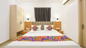 A hotel room with a bed, a wardrobe, a bedside table with a lamp, and an air conditioning unit. - Fabhotel Moro Gujranwala Town (New Delhi)
