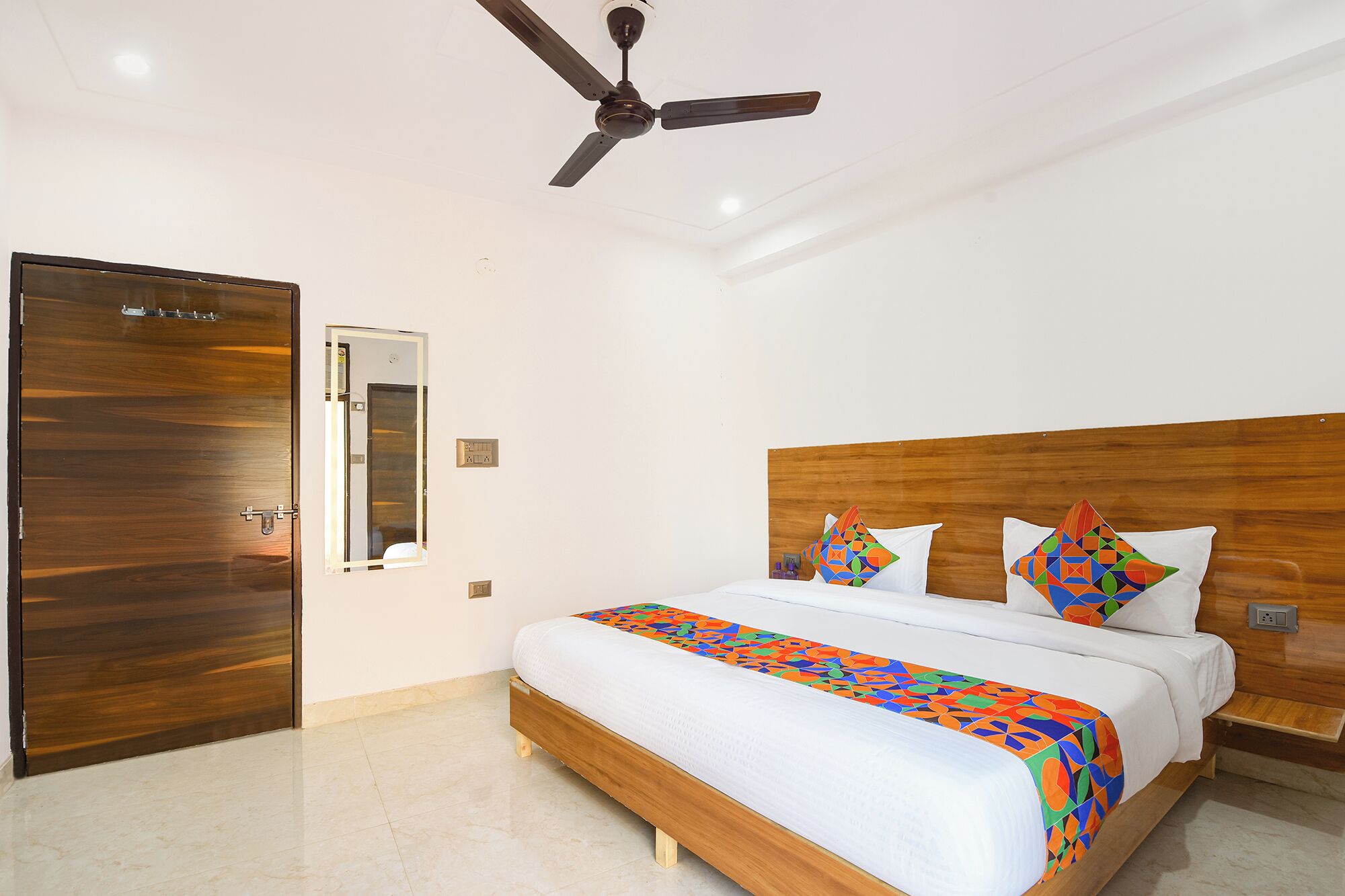Quarto com cama de madeira, ventoinha no teto, espelho e porta.