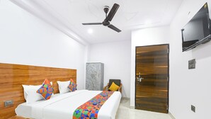 Habitación de hotel con cama, cabecera de madera, ventilador de techo, televisor montado en la pared y una puerta.