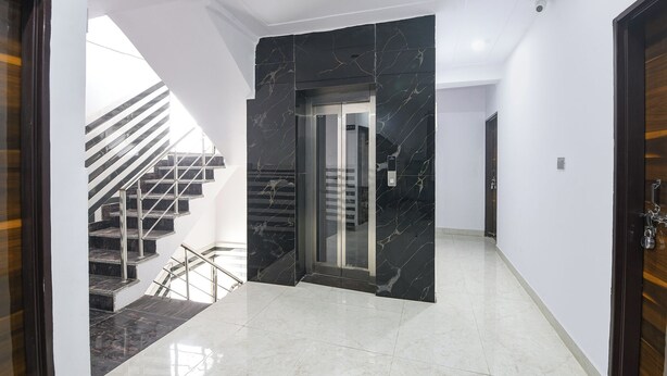 Un interior moderno con un ascensor de mármol, una escalera con barandilla metálica y un piso blanco y pulido.