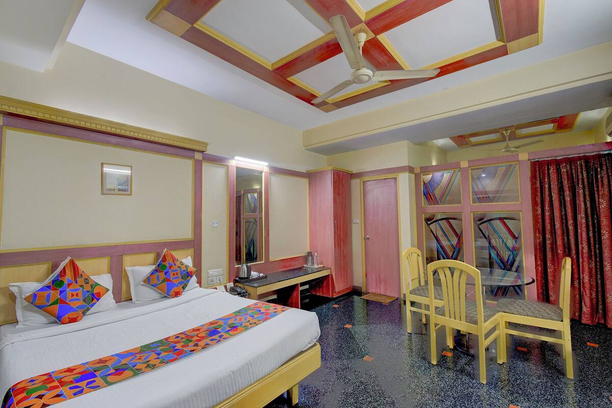 Habitación de hotel con cama, escritorio, silla, ventilador de techo y ventana con cortinas.