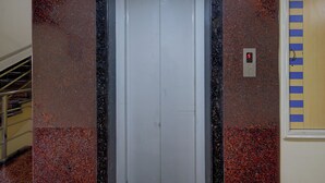 A white elevator door with a digital display showing the number 5, surrounded by a speckled red and black wall.