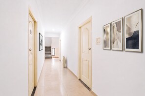Ein Flur mit Fliesenboden, einer Treppe im Hintergrund und drei gerahmten Kunstwerken an der Wand.