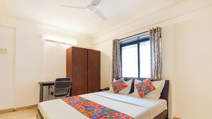 A hotel room with a bed, a desk, a wardrobe, and a window with patterned curtains. - Fabhotel Ateethi Residency (Pune)