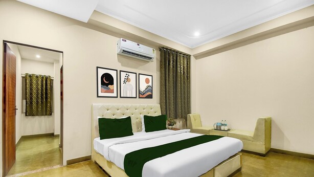 A hotel room with a bed, a mirror, a window with curtains, an air conditioning unit, and framed artwork on the wall. - FabHotel Runway, Near Jawahar Circle - Patrika Gate (Jaipur)