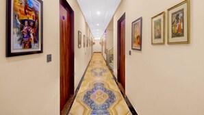 A hallway with framed artwork on the walls, a marble patterned floor, and a staircase at the end. - FabHotel Runway, Near Jawahar Circle - Patrika Gate (Jaipur)