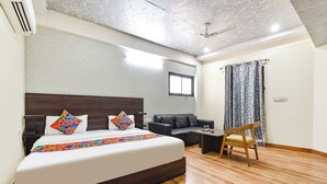 Camera d'albergo con un letto, un divano, una sedia di legno, una ventola a soffitto e una finestra con tende.