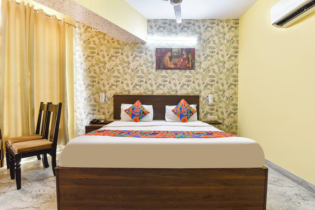 Habitación de hotel con cama, una silla, una mesita de noche, aire acondicionado instalado en la pared y ventilador de techo.