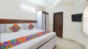 A hotel room with a bed, a ceiling fan, a TV, and a wardrobe. - Via Chahal (New Delhi)