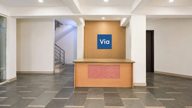 A reception desk with a 'Via' sign, a staircase, and a door in a modern lobby. - Via Chahal (New Delhi)