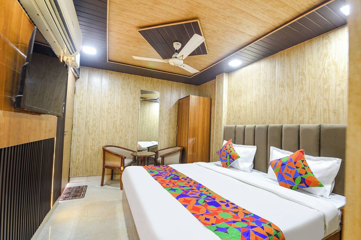 Quarto de hotel com cama, escrivaninha, cadeira, televisão e ventoinha no teto.