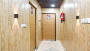 A hallway with wooden walls, a fire extinguisher, and a door with a number sign. - Via The Akshardham Bliss - LAXMI NAGAR METRO (New Delhi)