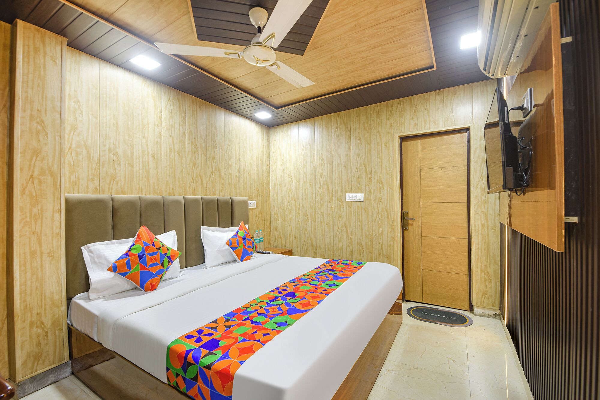 A hotel room with a bed, a ceiling fan, wooden walls, and a shower room sign.