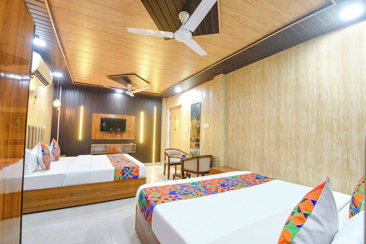 Quarto de hotel com duas camas, uma televisão, um ventilador de teto e uma pequena mesa.