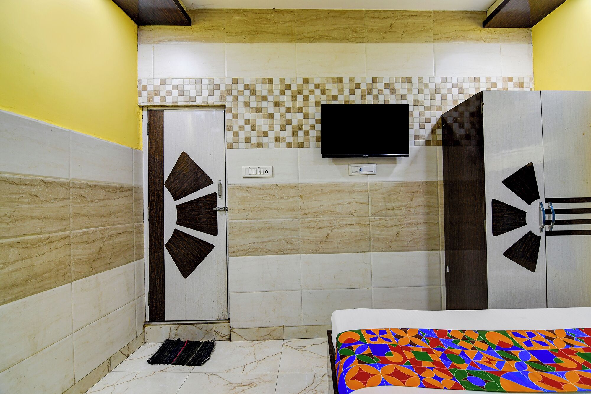 Quarto de hotel com uma cama, uma televisão fixada na parede e uma porta com design geométrico.