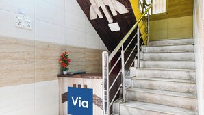 A staircase with a metal handrail, a potted plant, and a sign with the word 'Via' on a blue background.