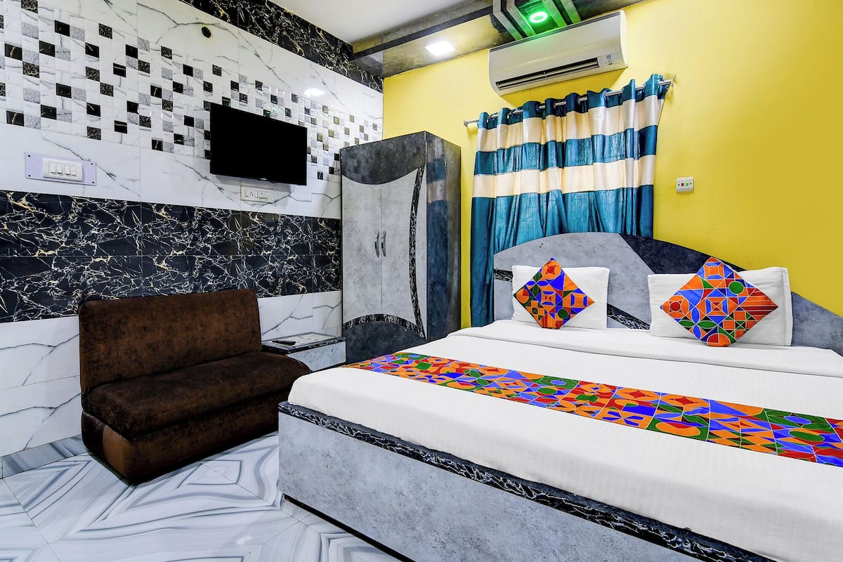 A hotel room with a bed, a brown armchair, a flat-screen TV, and a shower area.