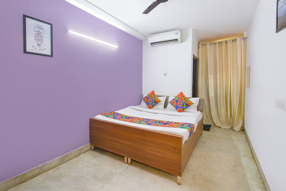 A bedroom with a bed, a ceiling fan, an air conditioner, and a window with curtains.