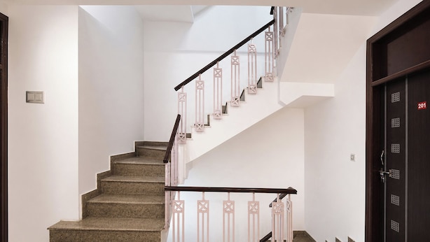 A staircase with a handrail, carpeted steps, and a door with a number plate. - Via A Square Residency (New Delhi)