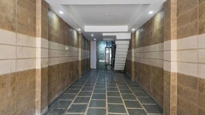 A hallway with patterned walls and a tiled floor, leading to a door with a glass panel. - Via Vsr Stay (New Delhi)