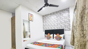 A bedroom with a bed, a ceiling fan, a mirror, and a floral-patterned wall. - Via Vsr Stay (New Delhi)