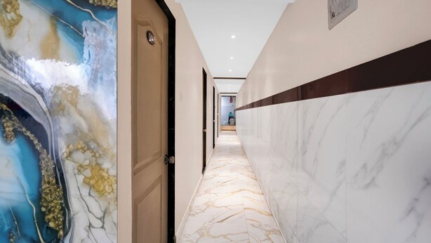 A hallway with a marble floor, a door with a number plate, and a wall with a decorative mural. - Via Shera Residency (Mumbai)