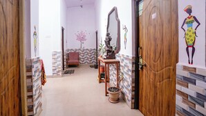 Un pasillo con puertas de madera, un espejo, una estatua y un árbol decorativo en la pared.