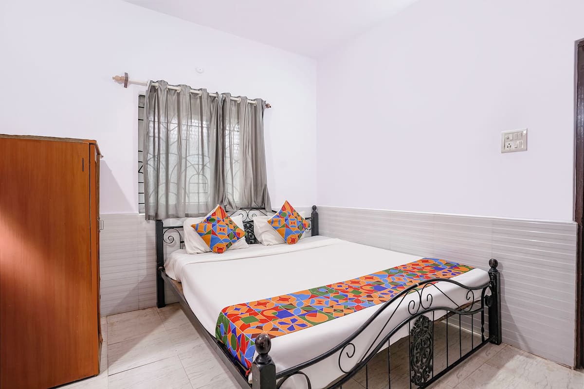 Un dormitorio con cama, cortinas, un armario de madera y suelo de baldosas.