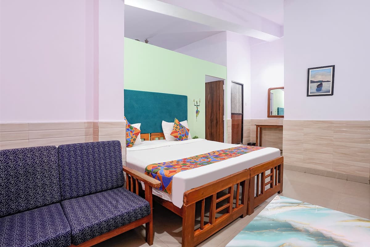 Una habitación con cama, sofá, banca de madera, espejo y un cuadro en la pared.