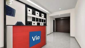 A reception desk with a 'Via' logo, a black and white shelving unit, and a closed door in the background. - Via Cosy Stay (New Delhi)