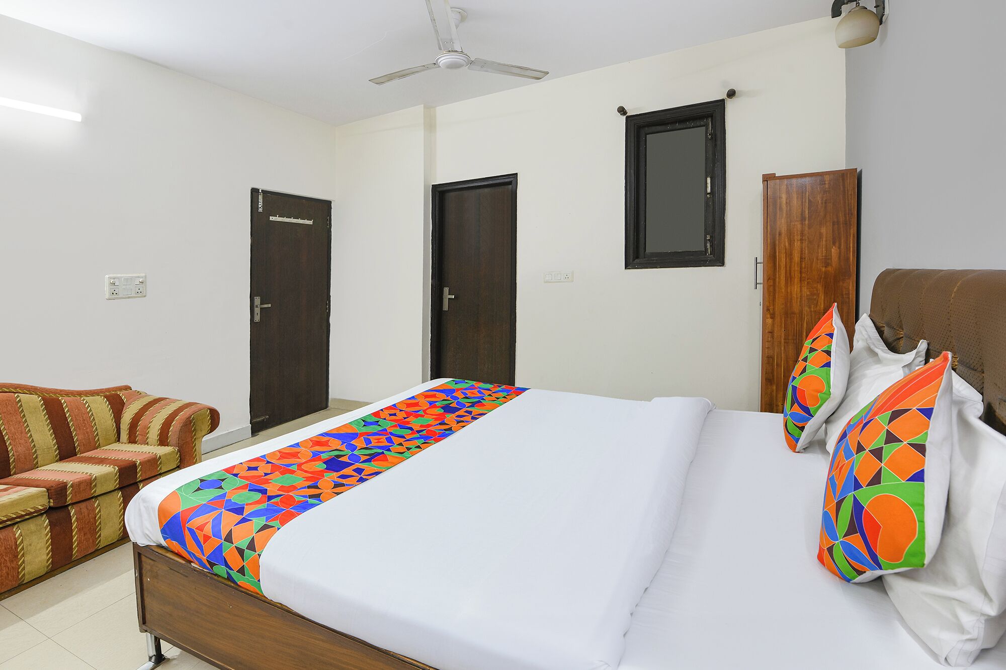 A hotel room with a bed, a sofa, two doors, a ceiling fan, and a window.